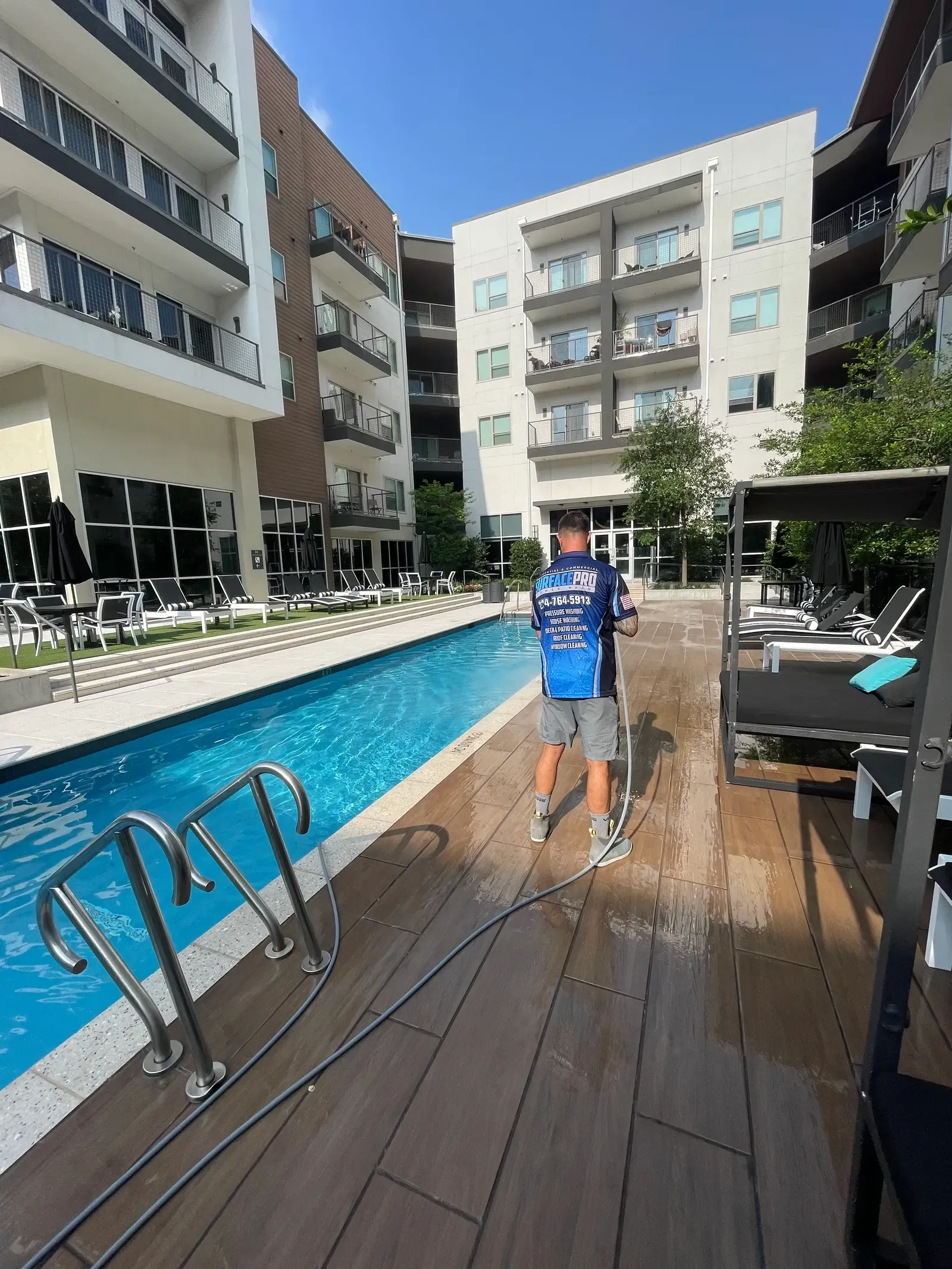 Technician rinsing a tile pool deck at an apartment community amenity pool in Frisco, TX