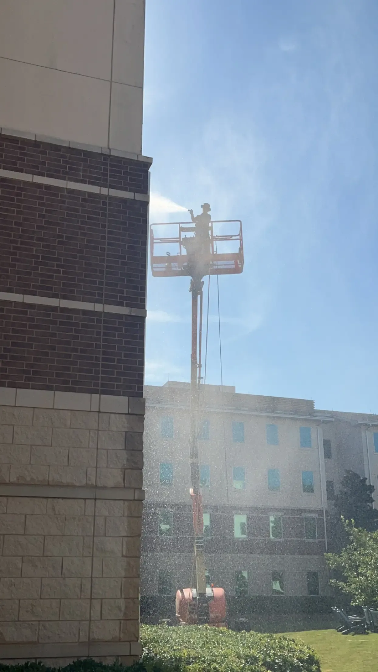 Technician soft washing a brick and cast stone facade from a boom lift in Allen, TX