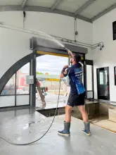 Technician pressure washing a commercial overhead door bay during post construction cleanup in Allen, TX