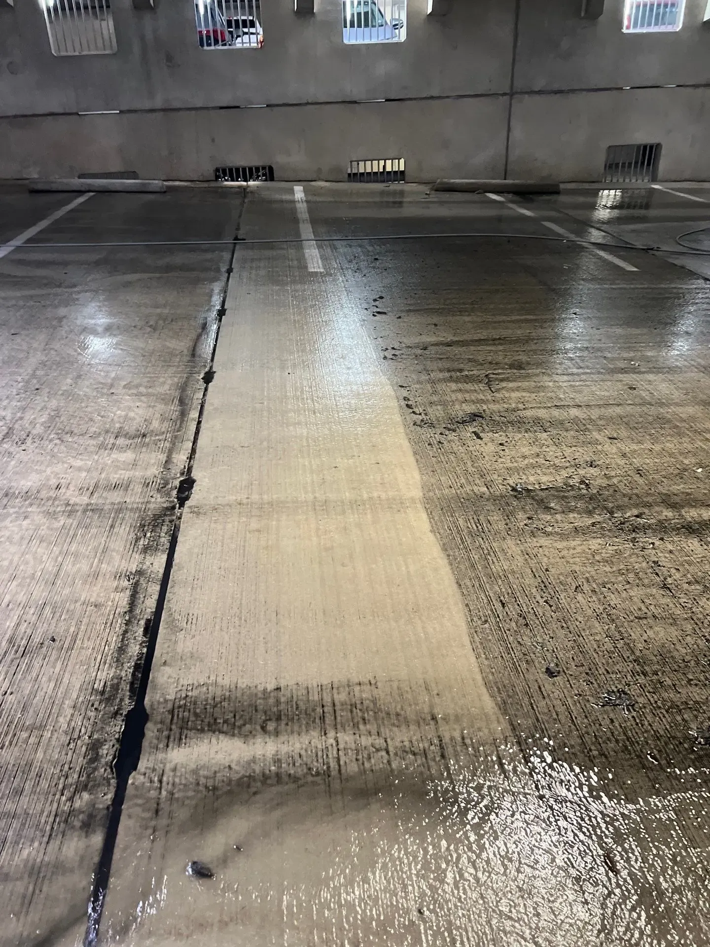Single cleaned strip of concrete contrasting with surrounding grime on a parking garage floor in Plano, TX