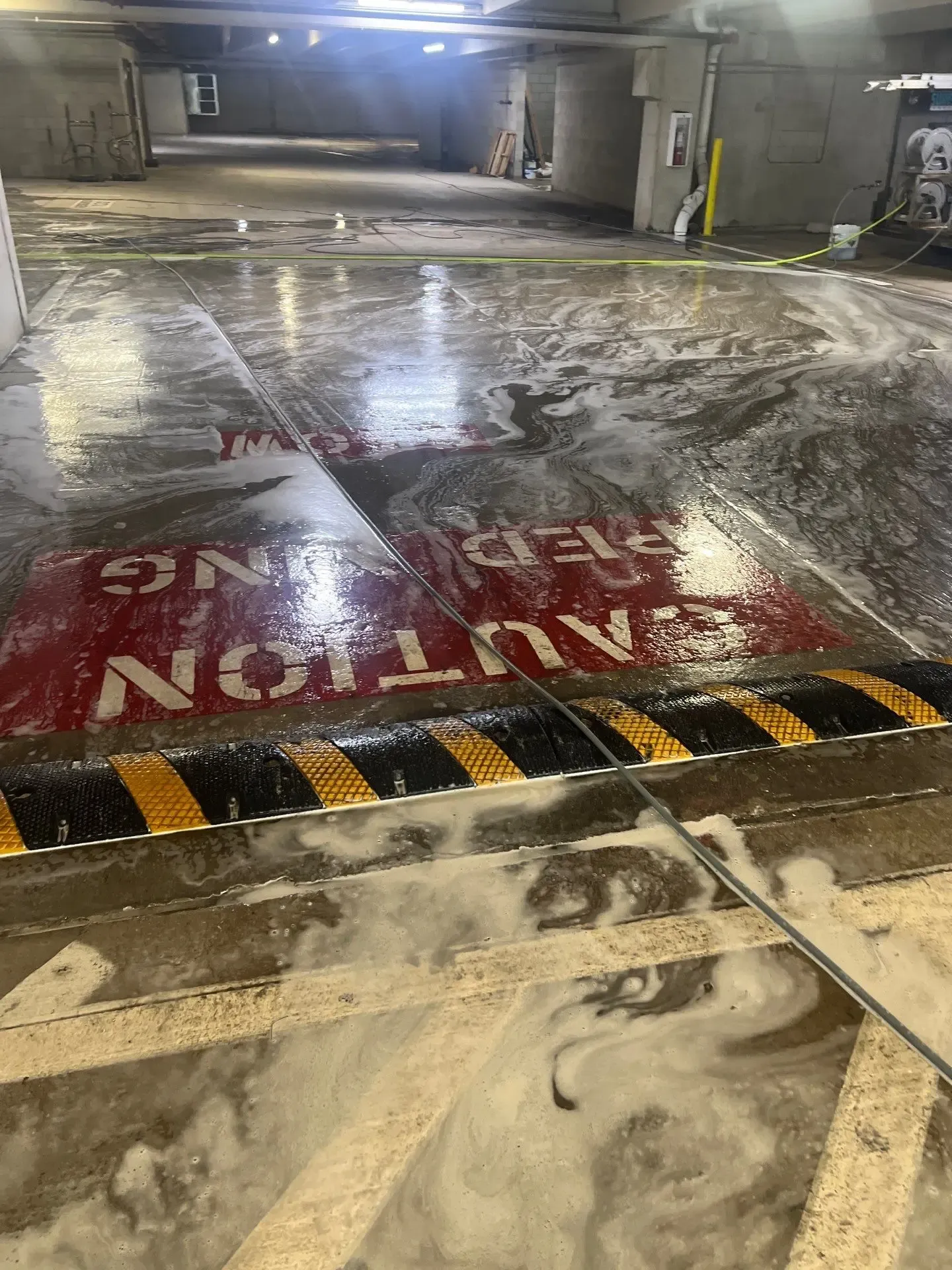 Detergent foam working across a parking garage concrete floor during pressure washing in Allen, TX
