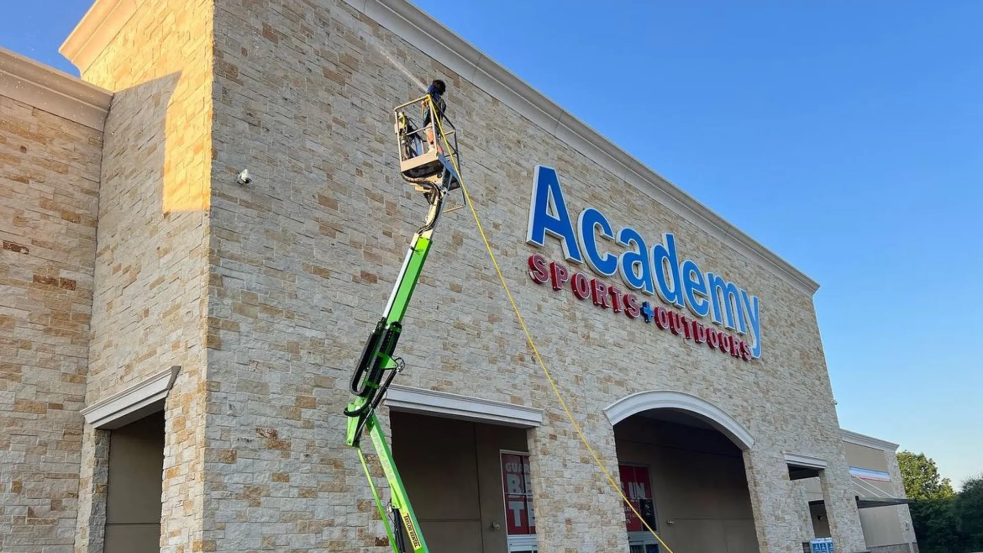 Surface Pro Power Wash technician cleaning the Academy Sports and Outdoors building exterior from a boom lift