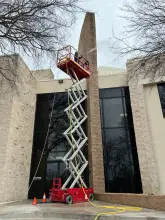 Technician on a scissor lift pressure washing a stone office building facade in Frisco, TX