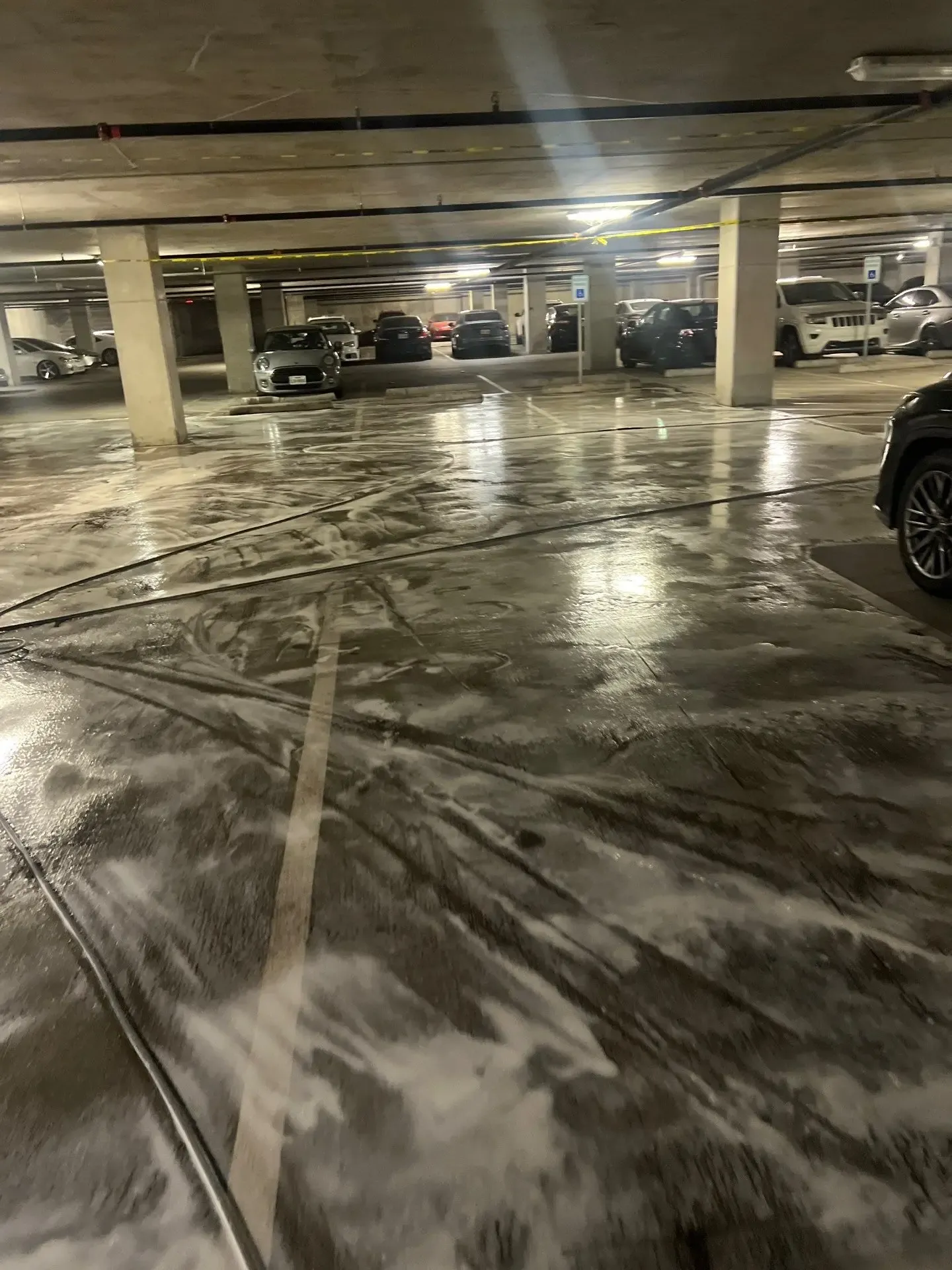 Detergent foam working on parking garage concrete between parked cars during cleaning in Dallas, TX