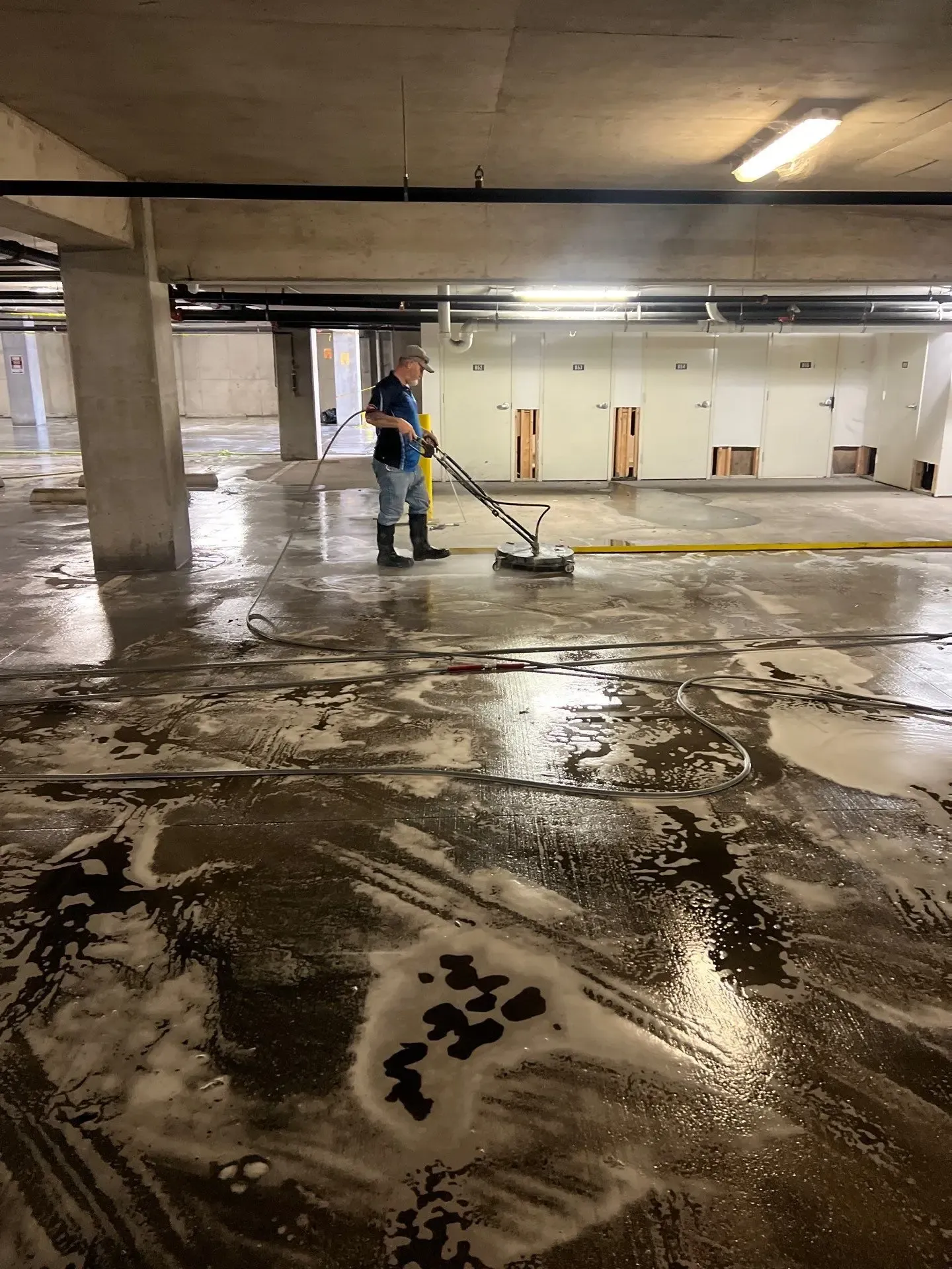 Technician deep cleaning parking garage concrete with a rotary surface cleaner and detergent in Richardson, TX
