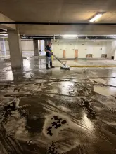 Technician deep cleaning parking garage concrete with a rotary surface cleaner and detergent in Richardson, TX