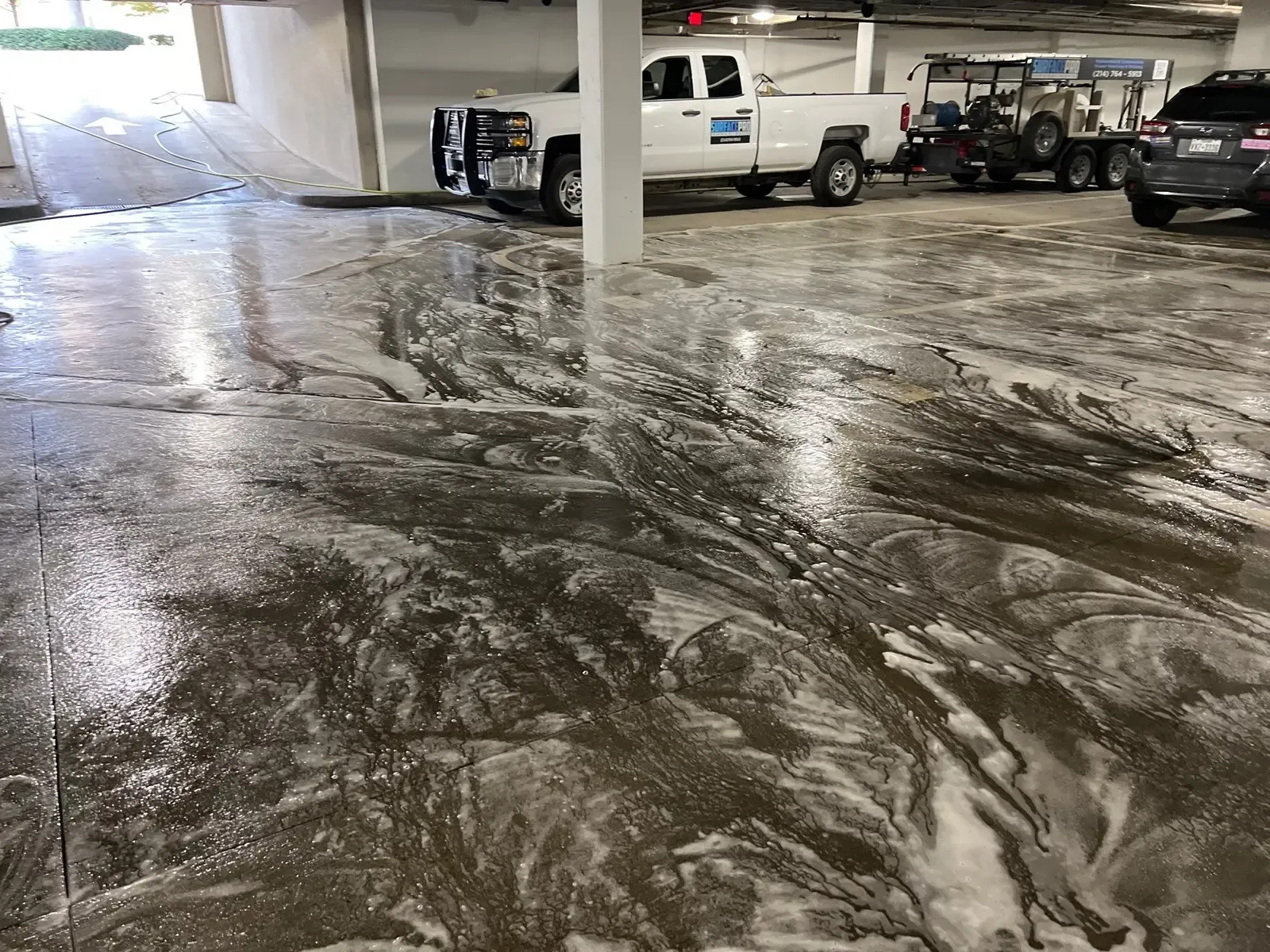 Pressure washing truck and trailer rig staged in a parking garage with detergent on the concrete in Richardson, TX