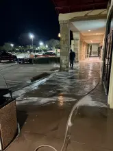Technician rinsing a shopping center sidewalk during an overnight pressure washing job with the wash rig staged nearby in Frisco, TX