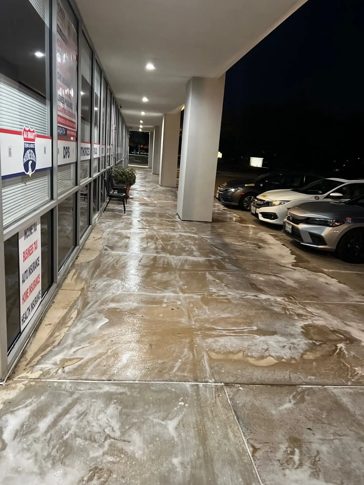 Cleaning solution dwelling on a commercial storefront sidewalk during an overnight concrete cleaning service in Dallas, TX